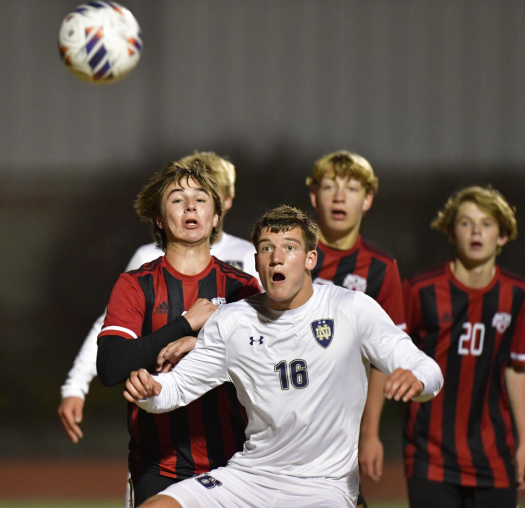 Quincy Notre Dame defender Deakon Schuette (right) eyes an incoming ball in the air as he jostles with Timothy Christian midfielder Jake Firnsin. Quincy Notre Dame defeated Timothy Christian 4-1 in a semifinal game of the Class 1A state soccer tournament at the East Side Centre in East Peoria, IL on Friday October 28, 2022.  
Photo Courtesy Tim Vizer Photography