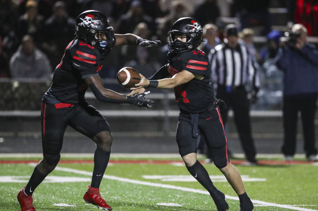 Hannibal’s Waylon Anders (14) hands the ball to Mike Ferreira (28) during the Hannibal Pirates district championship game against the Warrenton Warriors, Friday in Hannibal.  Mathew Kirby (Herald WhigCourier Post)